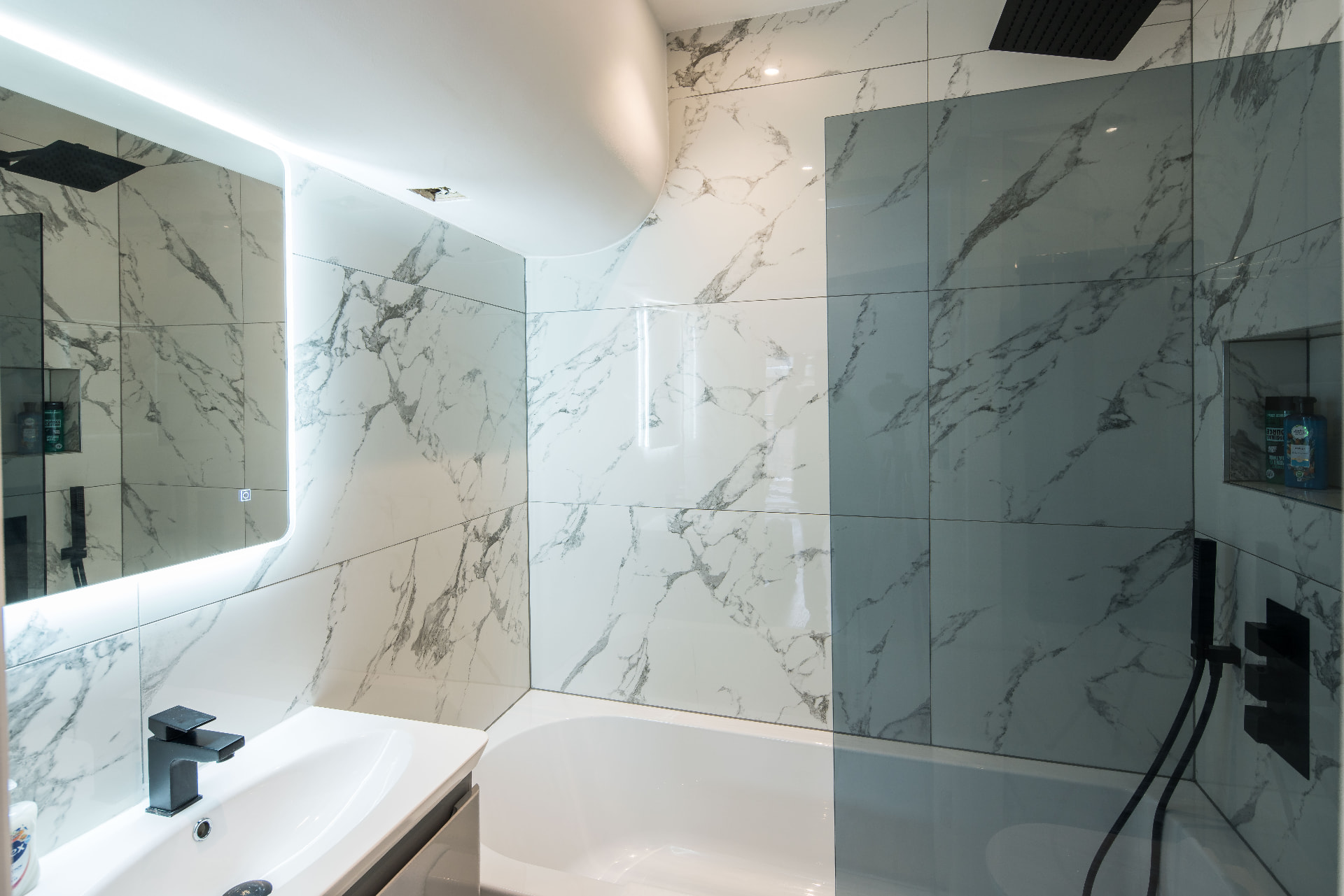 Bathroom finished in marble-patterned tiling with black fittings.